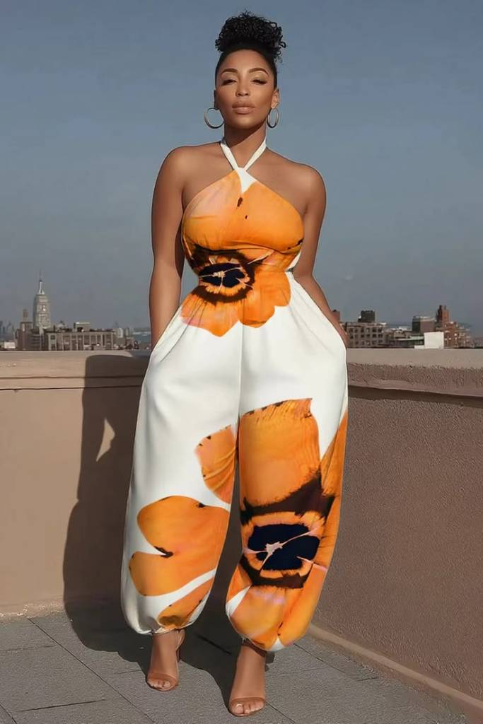 A woman wearing a halter neck jumpsuit with large orange flower patterns, standing on a rooftop with a city skyline in the background.